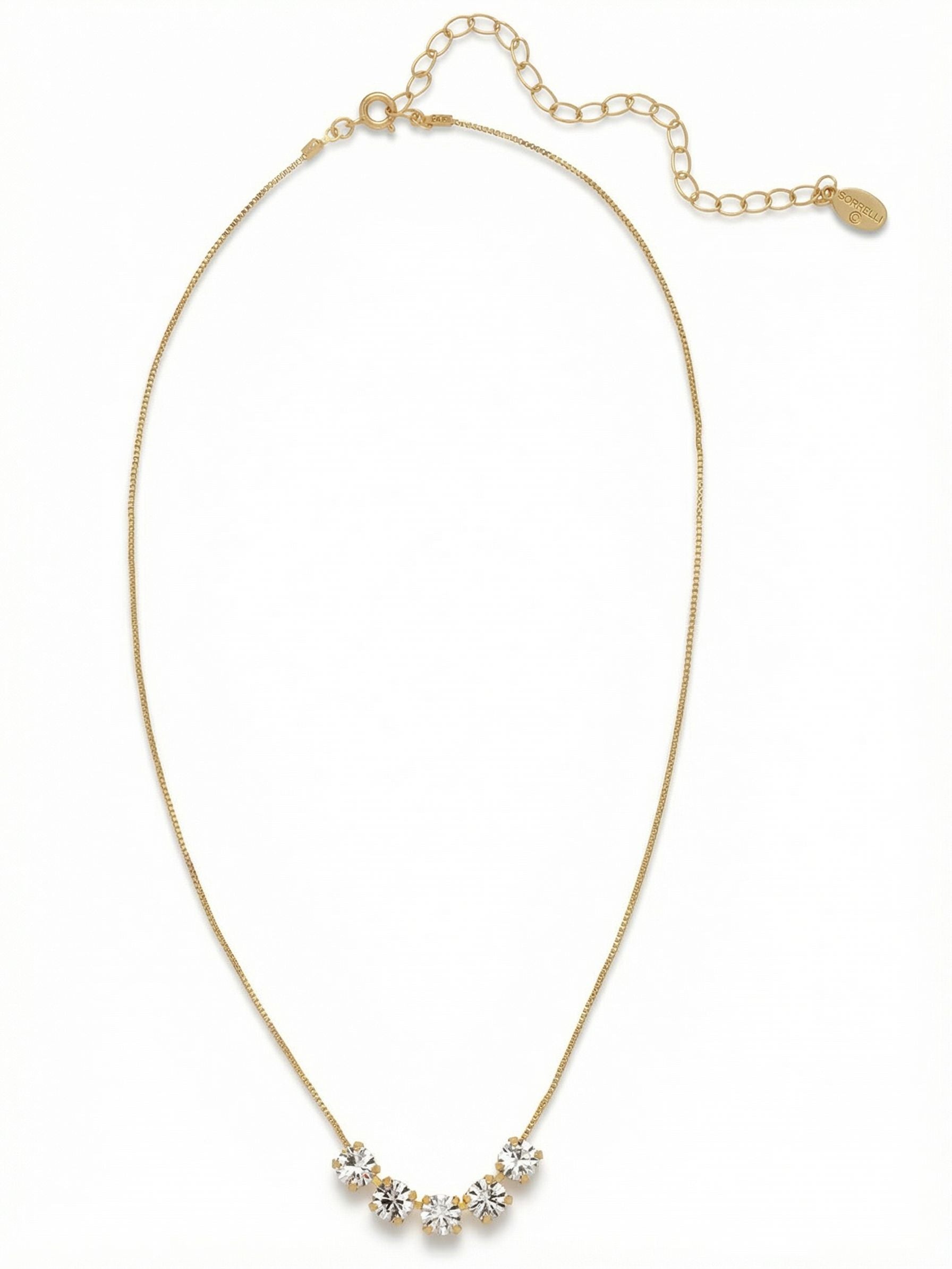 Shaughna Tennis Necklace - NFC84BGCRY - <p>Five round-cut clear crystals trace the hollow of your throat, suspended securely on a fine gold-tone chain. The design distills the traditional tennis necklace into a subtle, everyday focal point. These center stones catch ambient light as you move, while the delicate chain keeps the overall weight completely effortless. An adjustable extension link lets you place the crystals precisely where they suit your neckline most, making it an intuitive anchor for building a layered look.</p><ul>
<li>Five round-cut clear crystals clustered at the center</li>
<li>Ultra-fine chain construction for a lightweight effect</li>
<li>Lobster claw clasp</li>
<li>4-inch adjustable extension chain</li>
<li>Protective e-coat finish for lasting wear</li>
<li>Includes signature organza pouch for gifting and travel</li>
</ul>