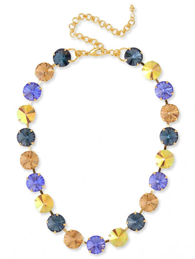 Nadine Tennis Necklace - NFU3BGDNM - <p>Substantial round crystals bring immediate presence to the collarbone. Deep indigo and sapphire tones shift into warm amber and iridescent gold, creating a rhythm of color that catches light as you move. The half-inch stones are connected by a flexible channel chain, giving the heavy crystal weight a soft, fluid drape along the neckline. An included extension chain lets you adjust the drop, allowing it to frame a bare neckline or layer neatly over a fitted knit.</p><ul>
<li>Oversized round crystals create a bold collarbone statement</li>
<li>Alternating warm amber and deep blue tones offer a rich visual rhythm</li>
<li>Lobster claw clasp</li>
<li>4-inch adjustable extension chain</li>
<li>Protective e-coat finish for lasting wear</li>
<li>Includes signature organza pouch for gifting and travel</li>
</ul>