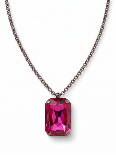 Viretta Pendant Necklace - NFZ16GMFU - <p>A singular, substantial emerald-cut crystal anchors this necklace, dropping cleanly from a fine rolo chain. The dark metal finish provides a quiet contrast to the vivid fuchsia stone, drawing the eye directly to its deep facets and architectural lines. The pendant carries a satisfying physical weight that grounds the delicate chain right at the collarbone. It stands as a confident focal point with enough presence to wear entirely on its own, while the extension chain lets you dial in the exact drop.</p><ul>
<li>Fine rolo chain contrasts with the heavy weight of the central focal stone</li>
<li>Prominent prong setting emphasizes the clean geometric lines of the emerald cut</li>
<li>Lobster claw clasp</li>
<li>4-inch adjustable extension chain</li>
<li>Includes signature organza pouch for gifting and travel</li>
</ul>