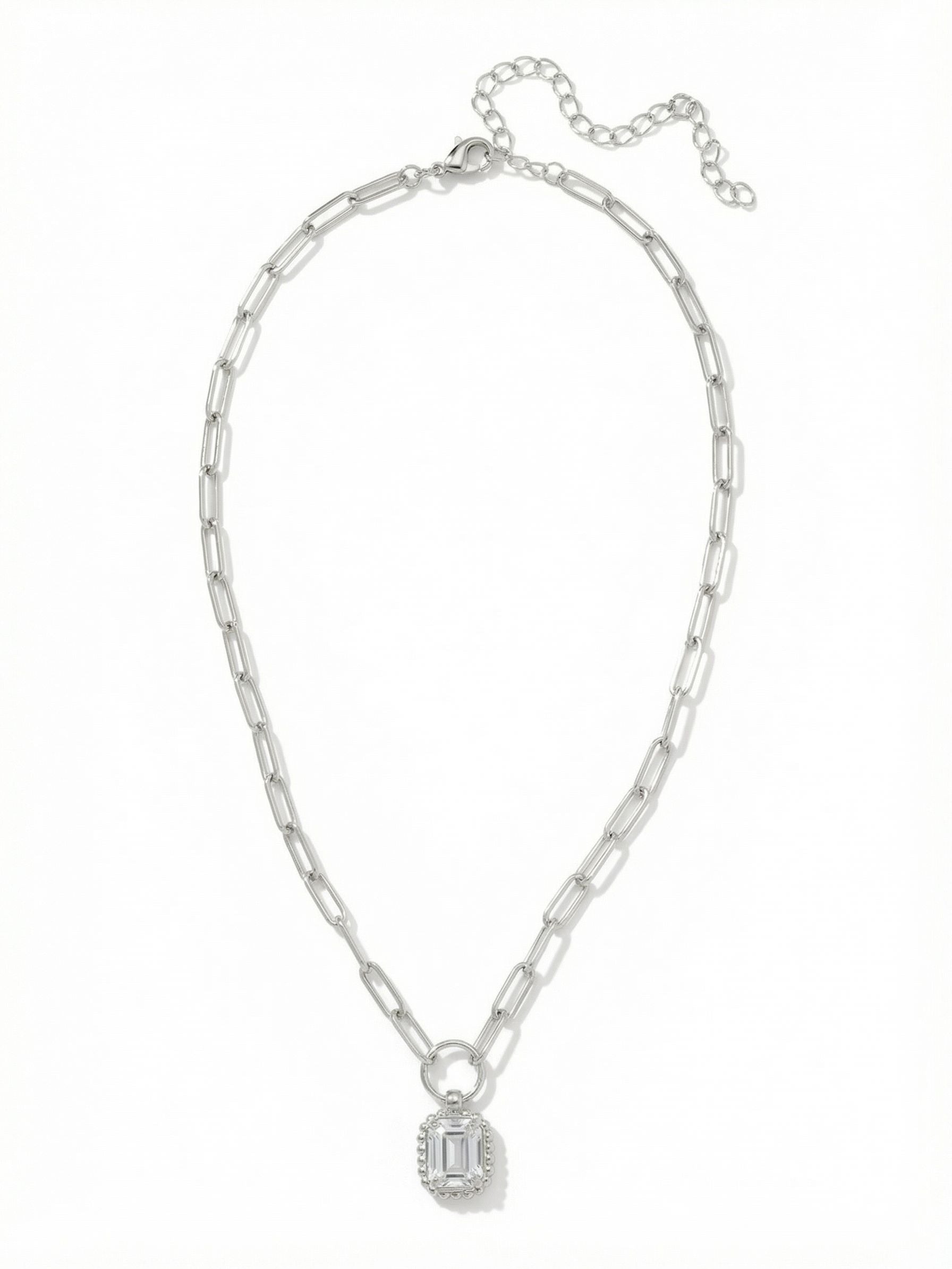 Octavia Scalloped Pendant Necklace - NGA1PDCRY - <p>A single emerald-cut clear crystal catches the light at the center of the collarbone. The stone is framed by a delicate scalloped border, suspended from an airy paperclip chain that adds a modern textural contrast to the classic pendant shape. Worn alone, it brings a quiet focal point to an open neckline. The attached extension chain allows you to adjust the drop, making it easy to layer with longer strands or tailor the fit to different collars.</p><ul>
<li>Single emerald-cut crystal framed by a beaded metal border</li>
<li>Open paperclip links provide a modern textural contrast</li>
<li>Lobster claw clasp</li>
<li>4-inch adjustable extension chain</li>
<li>Protective e-coat finish for lasting wear</li>
<li>Includes signature organza pouch for gifting and travel</li>
</ul>