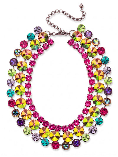 Penelope Layered Statement Necklace - NGB4GMNNI - <p>Three structured tiers of crystal fan outward across the collarbone in this wide statement piece. At the center, oversized iridescent stones shift between vibrant pinks and electric greens as you move. A saturated fuchsia inner rim creates a bright baseline, while the outer edge scatters contrasting hits of peridot, blue zircon, and rich burgundy. The dark gunmetal setting grounds the intense color palette, adding a moody undertone. Linked securely to maintain its shape, the necklace drapes evenly without flipping. The extension chain lets you adapt the drop for different necklines.</p><ul>
<li>Three-tiered kette chain construction prevents twisting and maintains the wide fan silhouette</li>
<li>Oversized central iridescent crystals framed by a saturated multicolor border</li>
<li>Lobster claw clasp</li>
<li>4-inch adjustable extension chain</li>
<li>Includes signature organza pouch for gifting and travel</li>
</ul>