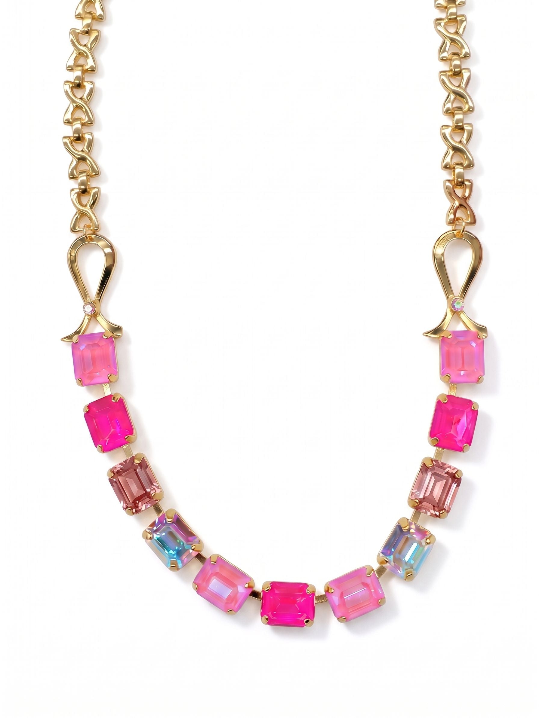 Ribbon of Hope Tennis Necklace - NGM2BGPIN - <p>A structured sweep of pink emerald-cut crystals frames the collarbone, held by sculpted gold-tone ribbon motifs. The stones transition through shades of soft rose and electric pink, punctuated by flashes of iridescence that catch ambient light. At the back, an open-link chain balances the profile, allowing the brightly colored center to take focus. The adjustable length lets you place the stones exactly where you want them, whether layered over a collar or framing bare skin.</p><ul>
<li>Emerald-cut crystals in shifting pink and iridescent tones</li>
<li>Sculpted metal ribbon motifs anchor an open-link chain</li>
<li>Lobster claw clasp</li>
<li>4-inch adjustable extension chain</li>
<li>Protective e-coat finish for lasting wear</li>
<li>Includes organza pouch for gifting and travel</li>
</ul>