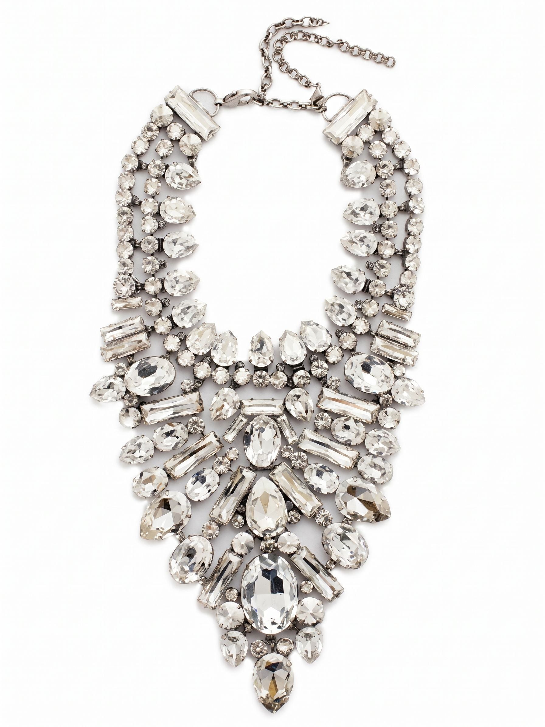 Crystal Cluster Statement Necklace - NSP80ASSSH - <p>This intricate bib necklace rests with deliberate weight across the collarbones, anchoring a deep plunge of meticulously arranged crystals. Seventeen distinct variations of pear, baguette, and oval stones create a textured, architectural piece that catches light from every angle. The foundation of ladder and channel chains allows the substantial design to articulate gently with your movements, preventing it from feeling rigid. Finished with an extension chain to dial in the drape perfectly, this piece commands the room with a quiet, icy confidence.</p><ul>
<li>Architectural mix of oval, pear, and baguette crystals creates a brilliant sunburst effect</li>
<li>Articulating ladder and channel chains allow the dense bib to move comfortably</li>
<li>Lobster claw clasp</li>
<li>Includes signature organza pouch for gifting and travel</li>
</ul>