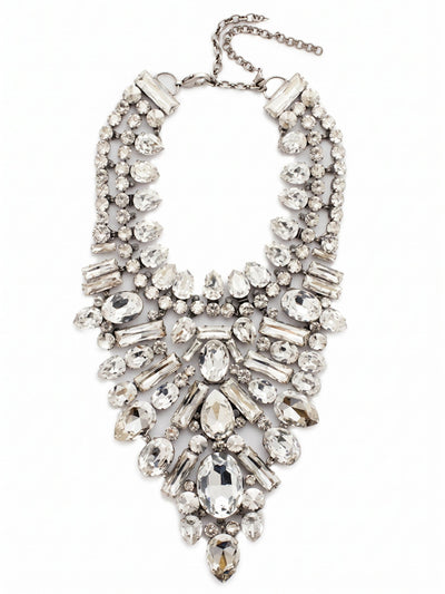 Crystal Cluster Statement Necklace - NSP80ASSSH - <p>This intricate bib necklace rests with deliberate weight across the collarbones, anchoring a deep plunge of meticulously arranged crystals. Seventeen distinct variations of pear, baguette, and oval stones create a textured, architectural piece that catches light from every angle. The foundation of ladder and channel chains allows the substantial design to articulate gently with your movements, preventing it from feeling rigid. Finished with an extension chain to dial in the drape perfectly, this piece commands the room with a quiet, icy confidence.</p><ul>
<li>Architectural mix of oval, pear, and baguette crystals creates a brilliant sunburst effect</li>
<li>Articulating ladder and channel chains allow the dense bib to move comfortably</li>
<li>Lobster claw clasp</li>
<li>Includes signature organza pouch for gifting and travel</li>
</ul>