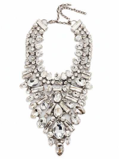 Crystal Cluster Statement Necklace - NSP80ASSSH - <p>This intricate bib necklace rests with deliberate weight across the collarbones, anchoring a deep plunge of meticulously arranged crystals. Seventeen distinct variations of pear, baguette, and oval stones create a textured, architectural piece that catches light from every angle. The foundation of ladder and channel chains allows the substantial design to articulate gently with your movements, preventing it from feeling rigid. Finished with an extension chain to dial in the drape perfectly, this piece commands the room with a quiet, icy confidence.</p><ul>
<li>Architectural mix of oval, pear, and baguette crystals creates a brilliant sunburst effect</li>
<li>Articulating ladder and channel chains allow the dense bib to move comfortably</li>
<li>Lobster claw clasp</li>
<li>Includes signature organza pouch for gifting and travel</li>
</ul>