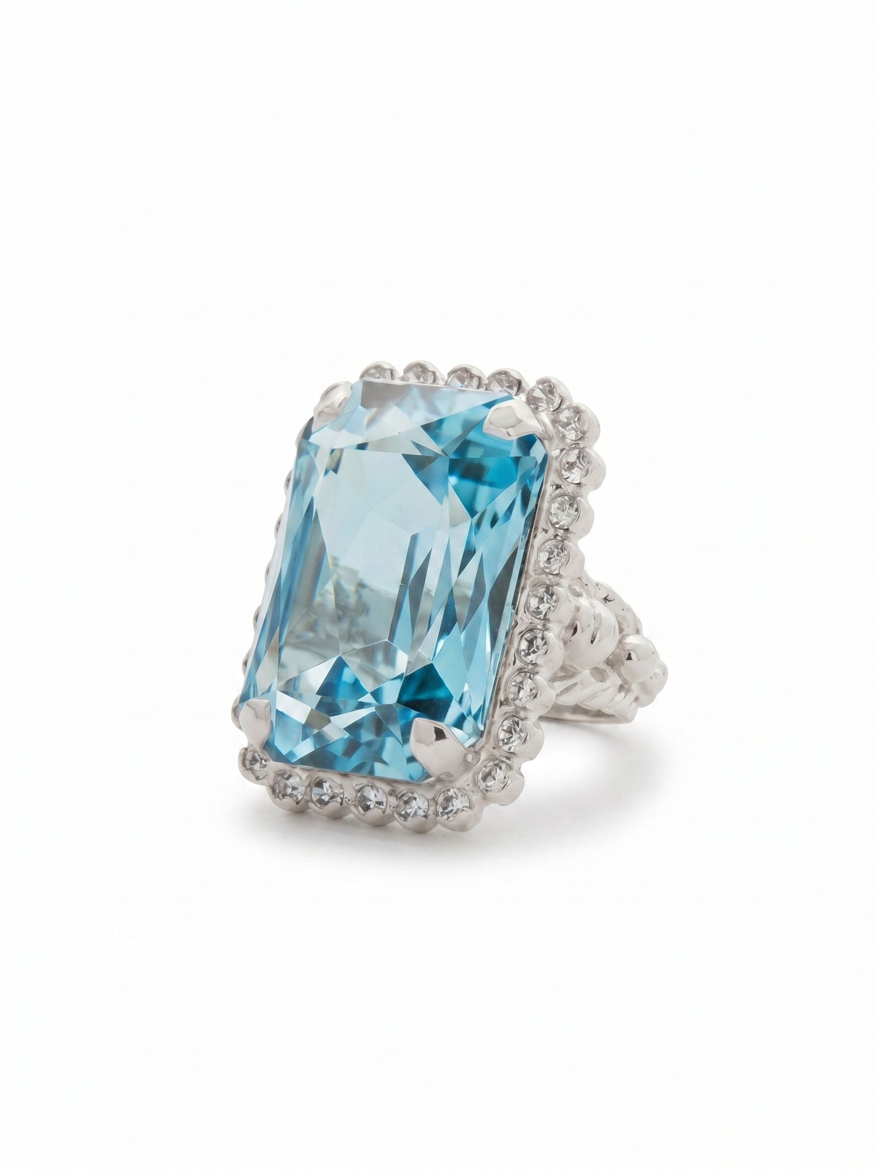 Luxurious Emerald-Cut Cocktail Ring - RBT69PDAQU - <p>A single substantial emerald-cut crystal anchors this cocktail ring, drawing the eye with deep facets that catch the light as you move your hands through the day. The pale aquamarine center is framed by a subtle border of clear rhinestones and ball chain detailing, giving the piece a grounded presence rather than overwhelming flash. Designed with an adjustable open band, it adapts easily to changes in temperature or a decision to wear it on a different finger.</p><ul>
<li>Oversized emerald-cut center stone framed by delicate crystal and ball chain accents</li>
<li>Elongated rectangular profile creates a pronounced visual presence on the hand</li>
<li>Adjustable ring band</li>
<li>Protective e-coat finish for lasting wear</li>
<li>Includes signature organza pouch for gifting and travel</li>
</ul>