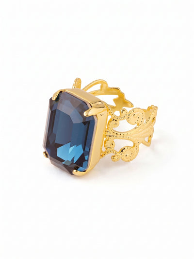 Brynn Cocktail Ring - RGK2BGMON - <p>An oversized emerald-cut crystal anchors this ring with deep, structured blue light that catches the eye during daily gestures. The stone is held securely above a wide openwork band detailed with intricate scrolling metalwork, giving the piece substantial visual weight without feeling heavy on the hand. An open back allows for gentle sizing adjustments, letting you shift the ring easily between fingers to suit your mood or the moment.</p><ul>
<li>Oversized emerald-cut crystal delivers a focused block of rich color</li>
<li>Wide openwork band detailed with intricate scrolling filigree metalwork</li>
<li>Adjustable ring band</li>
<li>Protective e-coat finish for lasting wear</li>
<li>Includes signature organza pouch for gifting and travel</li>
</ul>