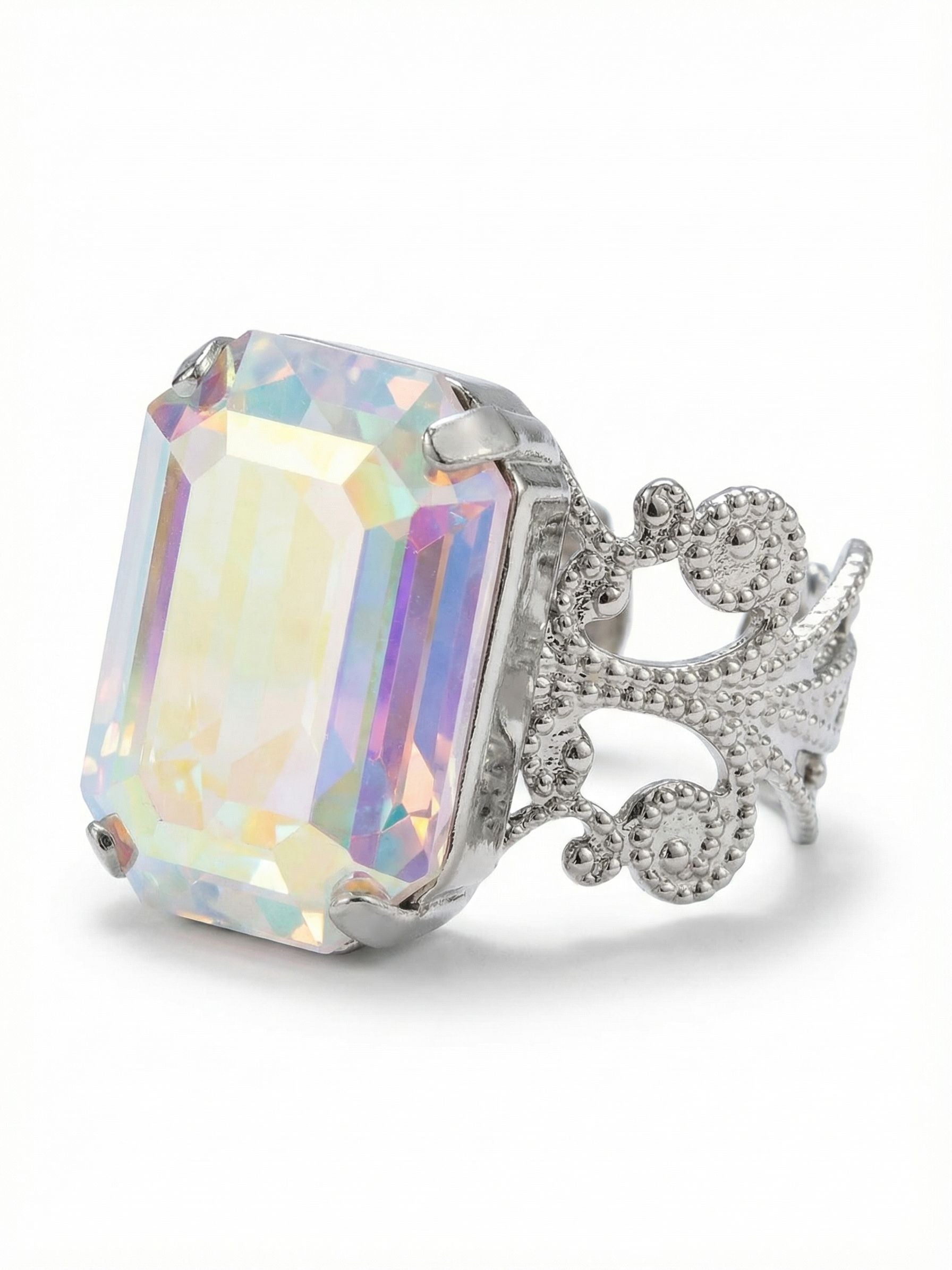Brynn Cocktail Ring - RGK2PDCAB - <p>A single, substantial emerald-cut crystal anchors this piece, capturing a shifting spectrum of pastel light as your hands move throughout the day. The iridescent quality of the stone contrasts with the structured geometry of the cut, creating a constant play of color and shadow. Set on an intricate filigree band with detailed metalwork, the ring balances clean lines with vintage-inspired craftsmanship. The open design easily adjusts to fit different fingers, adapting quietly to your routine.</p><ul>
<li>Substantial emerald-cut center stone offering broad facets of shifting pastel light</li>
<li>Ornate open-metalwork band with intricate textured detailing</li>
<li>Adjustable ring band</li>
<li>Protective e-coat finish for lasting wear</li>
<li>Includes signature organza pouch for gifting and travel</li>
</ul>
